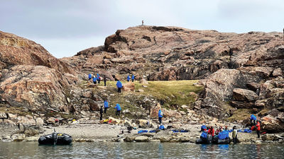 Adventure Canada guests set out to explore Devon Island, the largest uninhabited island in the world, as a spotter watches for polar bears from the top of a hill.